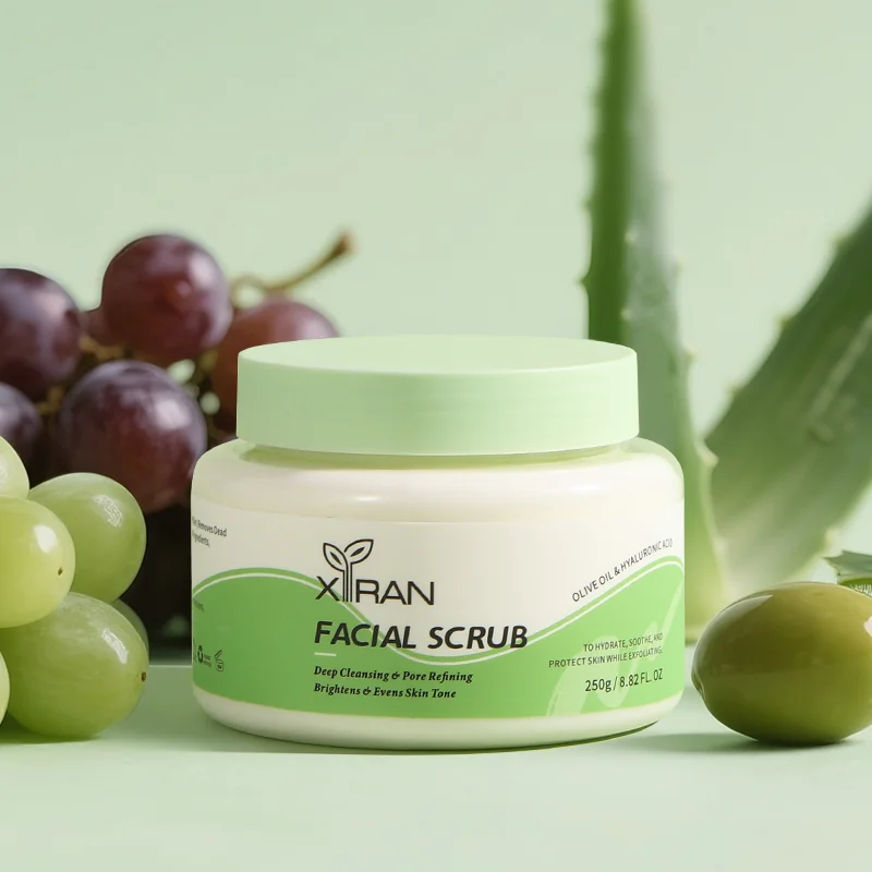 Xiran facial scrub in a jar with green lid, surrounded by grapes and aloe, highlighting natural ingredients.